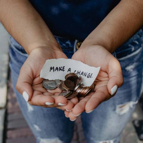 Hands holding a bunch of spare change with a note saying 'Make A Change'.